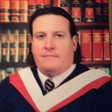 Man in graduation attire with bookshelf background.