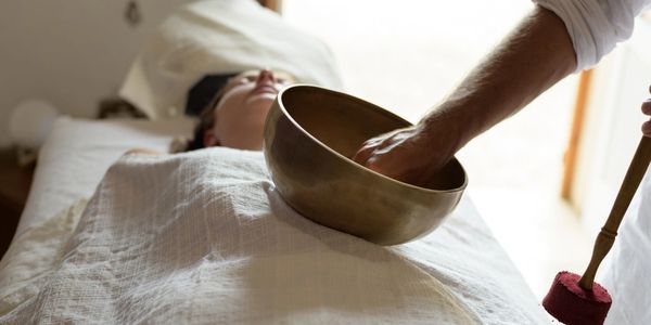 A person on a massage table with a sound practitioner using sound instrument on the body for healing
