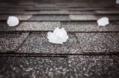 Large hailstones on a dark shingled roof after a hailstorm.