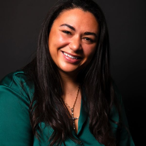 Smiling woman with long dark hair in a green blouse against a black background.