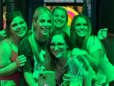 A group of five women smiling and posing closely together in green lighting.