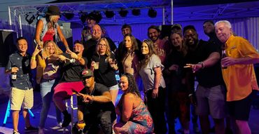 A lively group of friends enjoying a night out with drinks and music under blue lighting.