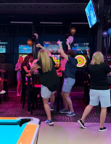 People enjoying a lively night at a bowling alley with colorful lights and balloons.