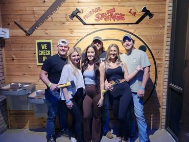 A group of six people posing with axes at Monroe Savage LA axe throwing venue.