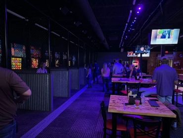 People enjoying axe throwing in a dimly lit venue with purple lighting.