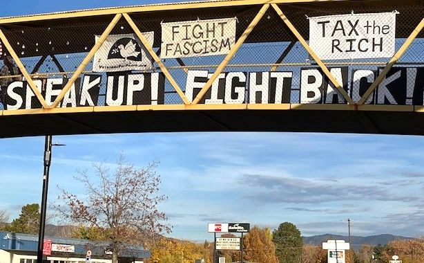 Protest signs on a pedestrian bridge urging to fight fascism and tax the rich.