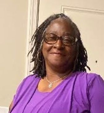 Woman smiling, wearing glasses and a purple top.