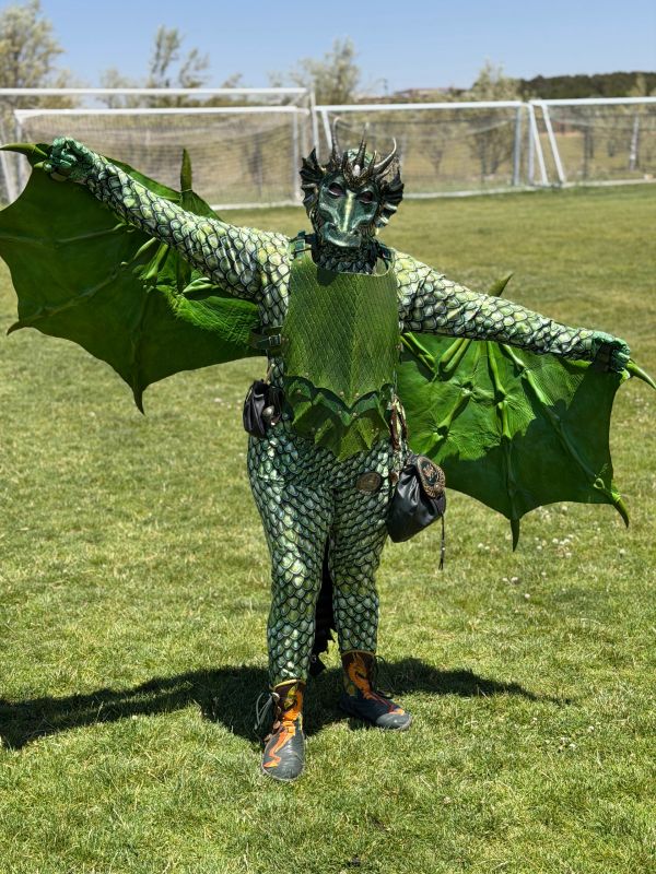 Person in a detailed green dragon costume with wings outdoors.