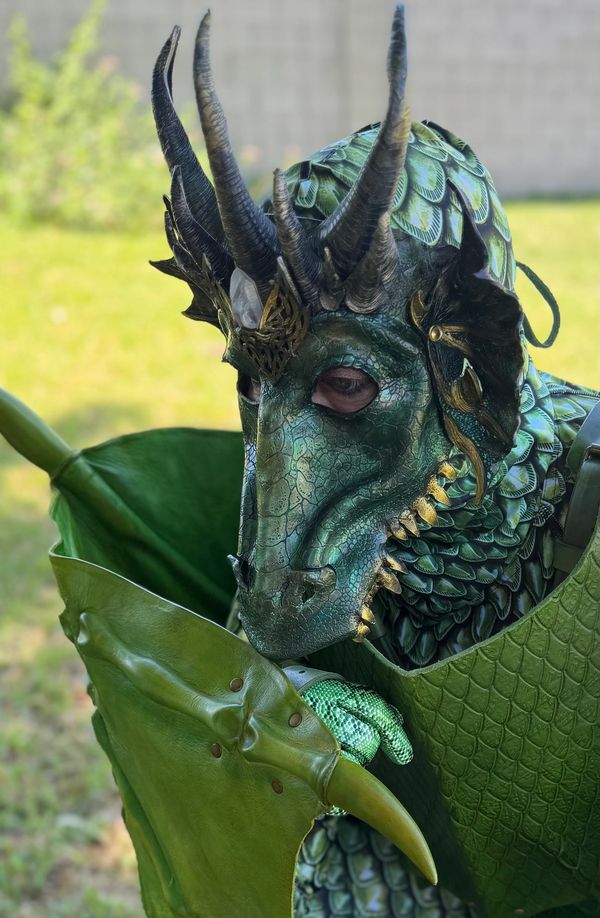 Person in detailed dragon costume with green scales and horns.