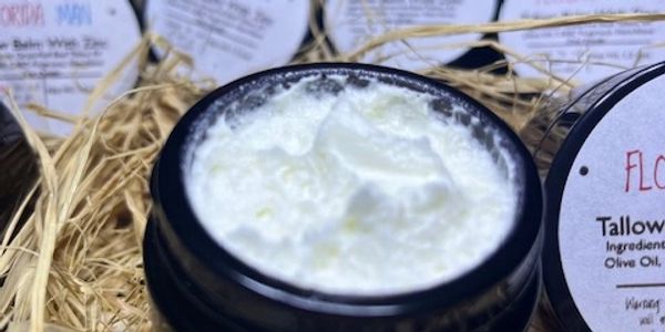 Open jar of creamy skincare product surrounded by similar jars in straw bedding.