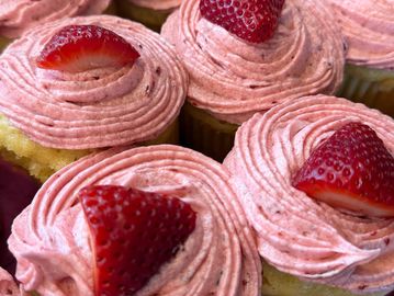 Cupcakes topped with pink frosting and fresh strawberry halves.