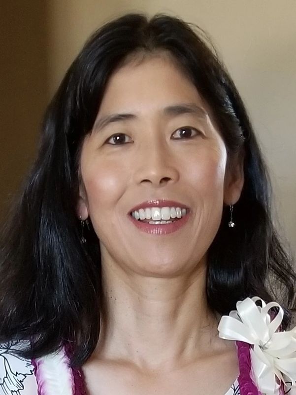 Smiling woman with long black hair and a white ribbon on her dress.