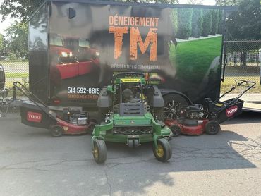 Three lawn mowers parked in front of a landscaping trailer.