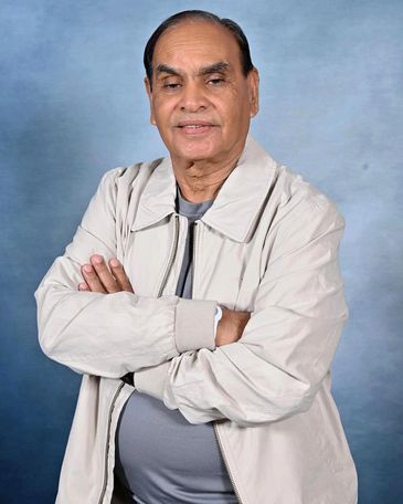 Elderly man with folded arms wearing a light jacket and gray shirt.