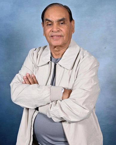 Elderly man with folded arms wearing a light jacket and gray shirt.