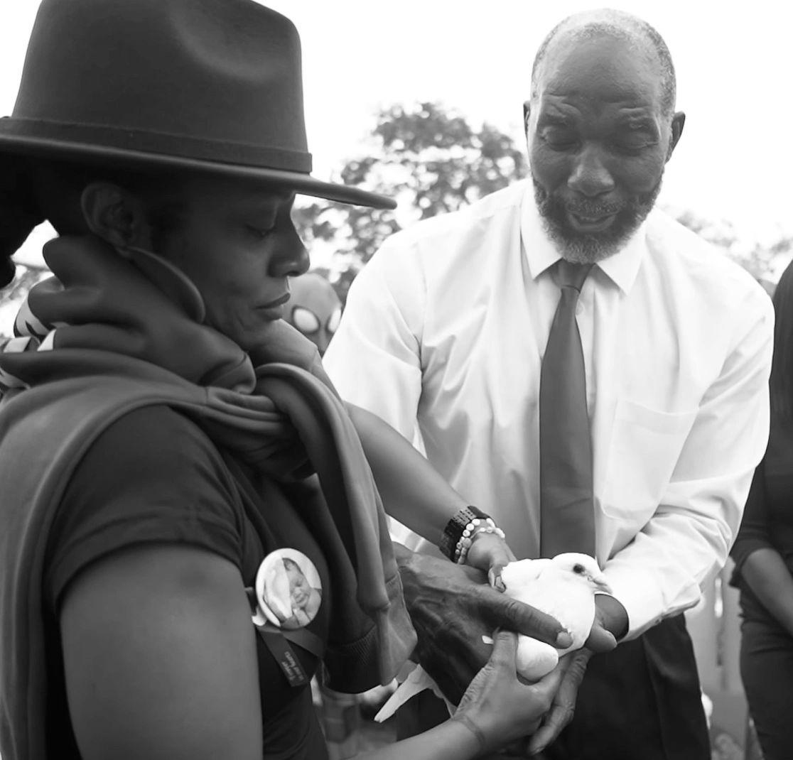 Two people gently holding a white dove during a solemn moment.