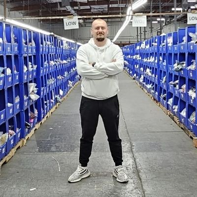 Man standing confidently in a warehouse aisle between blue shelves.