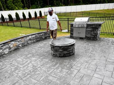 Man standing in a backyard patio with stone fire pit and built-in grill.