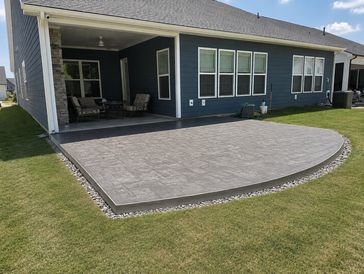 Newly installed concrete patio with stone border in backyard.