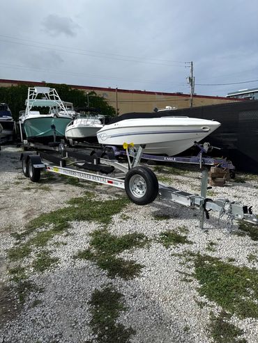 Boat trailer rental parked on gravel near several boats in a lot.