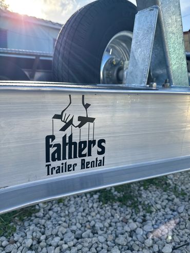 Close-up of a trailer with 'Fathers Trailer Rental' logo under sunlight.