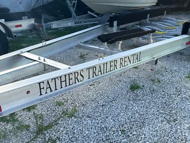 Boat trailers parked on a gravel lot outside a rental service.