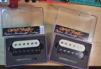 Two custom handmade guitar pickups in clear plastic cases on a workbench.