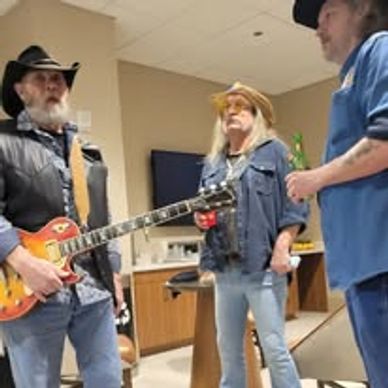 Three men in cowboy hats, one with a guitar, in a casual indoor setting.