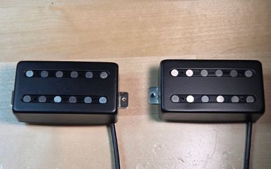 Two black electric guitar pickups with metal poles on a wooden surface.