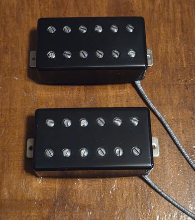 Two black guitar pickups with adjustable pole pieces on a wooden surface.