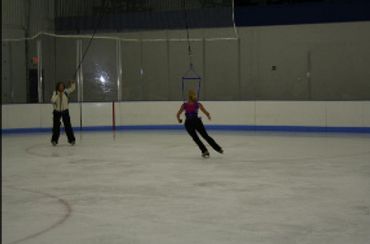 wide view of figure skaters using jump harnesses