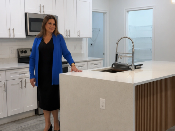 Woman standing in a modern kitchen with a blue cardigan.