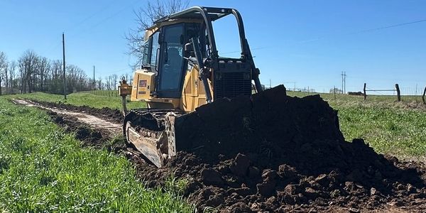 Bulldozer pushing soil on a dirt path in a rural area.