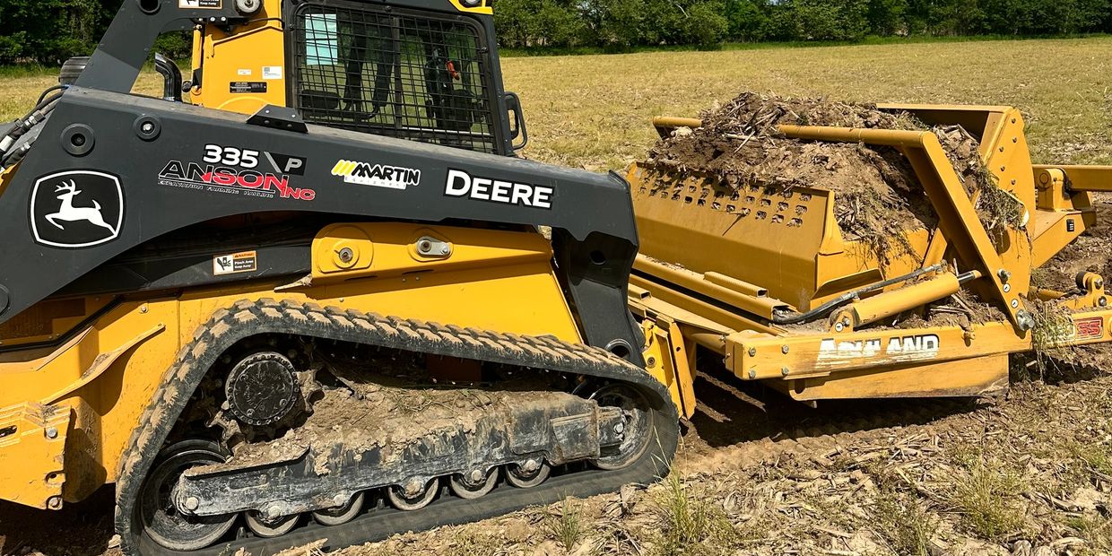 A John Deere 335 P tracked skid steer with an Ashland attachment filled with dirt.