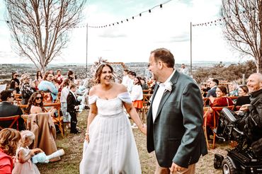 Joyful newlyweds walk hand in hand down the aisle during an outdoor wedding ceremony.