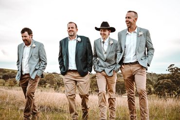 Four men in casual suits walking and laughing in a grassy field.
