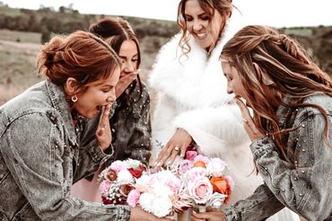 Bride and bridesmaids excitedly admiring bouquets and ring outdoors.