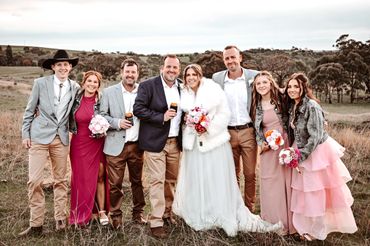 A joyful wedding group photo in a scenic outdoor setting with smiling friends and family.