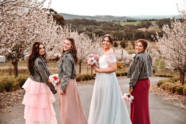 Bride and bridesmaids in elegant dresses and denim jackets among blooming trees.