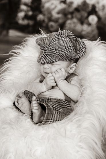 Newborn baby sleeping peacefully in a cozy fluffy chair, wearing a checkered hat and pants.