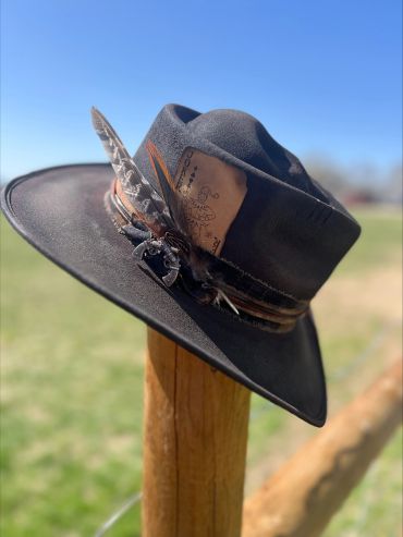 Black cowboy hat with feathers and a joker card tucked in the band.