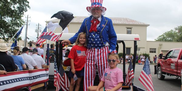 Man dressed as Uncle Sam poses on the back of a mule smiling with his grandchildren. 
