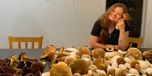 Woman happily posing with a large collection of mushrooms on a table.