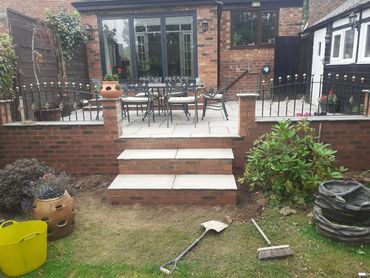 A backyard patio with brick steps, garden tools, and outdoor furniture.