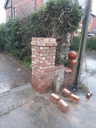 Freshly built brick pillar beside a hedge on a wet street corner.