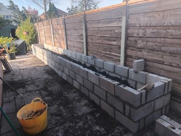 Long raised garden bed under construction with cinder blocks and soil inside.
