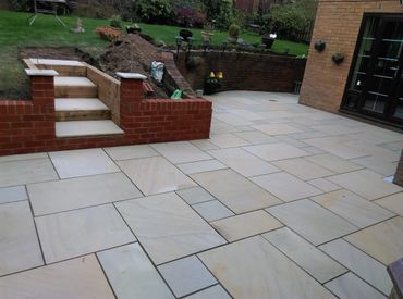 Newly paved backyard patio with stone tiles and brick steps leading to a garden.