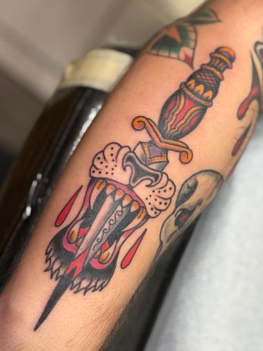 Traditional tattoo of a dagger stabbing a fierce dog face with blood drops.