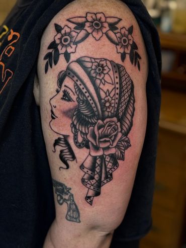 Tattoo of a vintage-style woman with flowers and a headscarf on an upper arm.