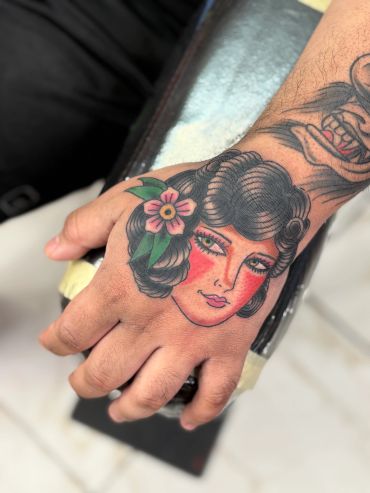 Tattoo of a woman's face with a flower on a hand.
